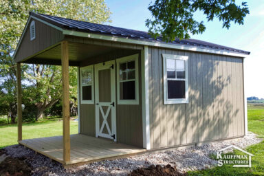 backyard utility shed with porch - taupe painted wood siding with white-trimmed single door with X detail and two windows on the front - a single window on the right side - brown metal roof