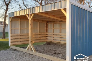 Blue painted metal loafing shed with white trim on farm with barren trees in near distance