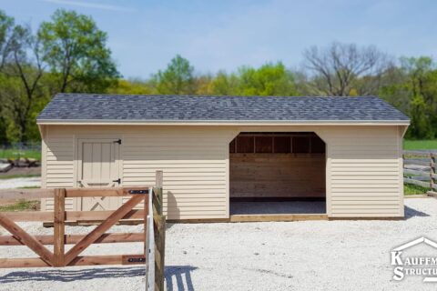 beige loafing shed with beige door left of animal entrance beneath dark gray shingled roof