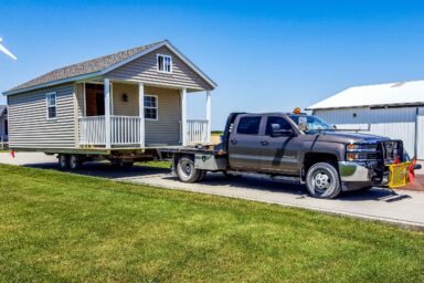 Large portable storage building being transported on a trailer by a truck on a sunny day - showcasing our professional shed moving services in Des Moines