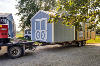 Blue-gray shed on a trailer of heavy-duty truck during shed moving.