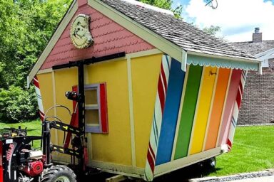 Colorful small shed with a rainbow pattern being moved with specialized equipment.