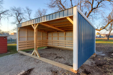 Blue-trim loafing shed with exposed wood framing and ground-level access.