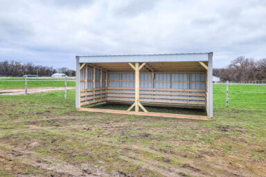 Compact loafing shed with open front and minimal framing in a grassy field.