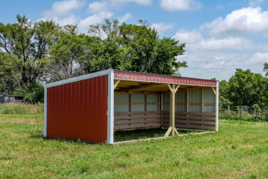 Red loafing shed with white trim placed in a sunny green field.