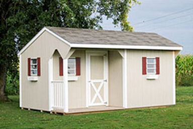 Backyard shed - eggshell siding with white-trimmed single door facing small partially fenced porch - three visible windows with burgundy shutters beneath brown shingled roof