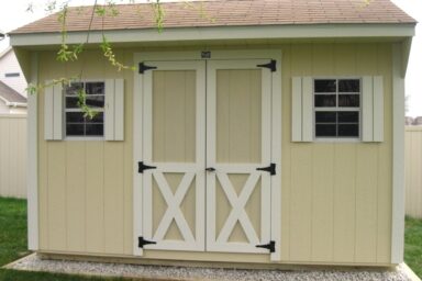 Backyard shed - eggshell siding with white-trimmed double doors and matching shutters on two windows beneath brown shingled roof