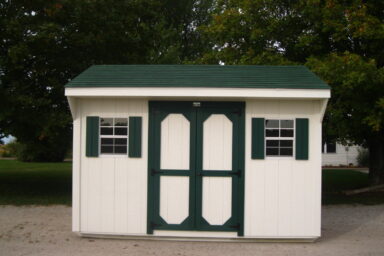 backyard shed with green-trimmed double doors and matching shutters on two windows under green shingled roof